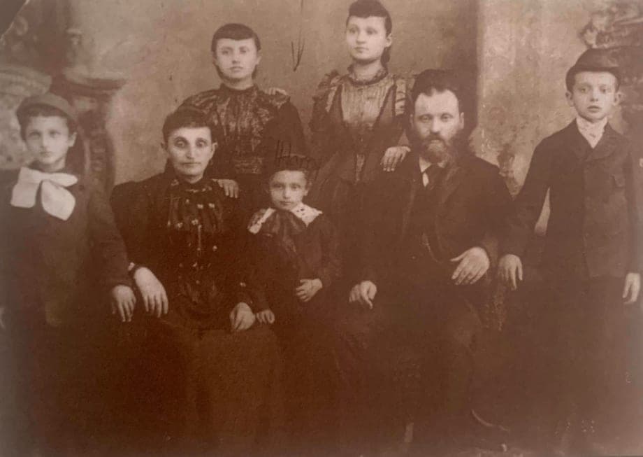 A sepia studio portrait of a family of seven — parents and five children — in formal dress