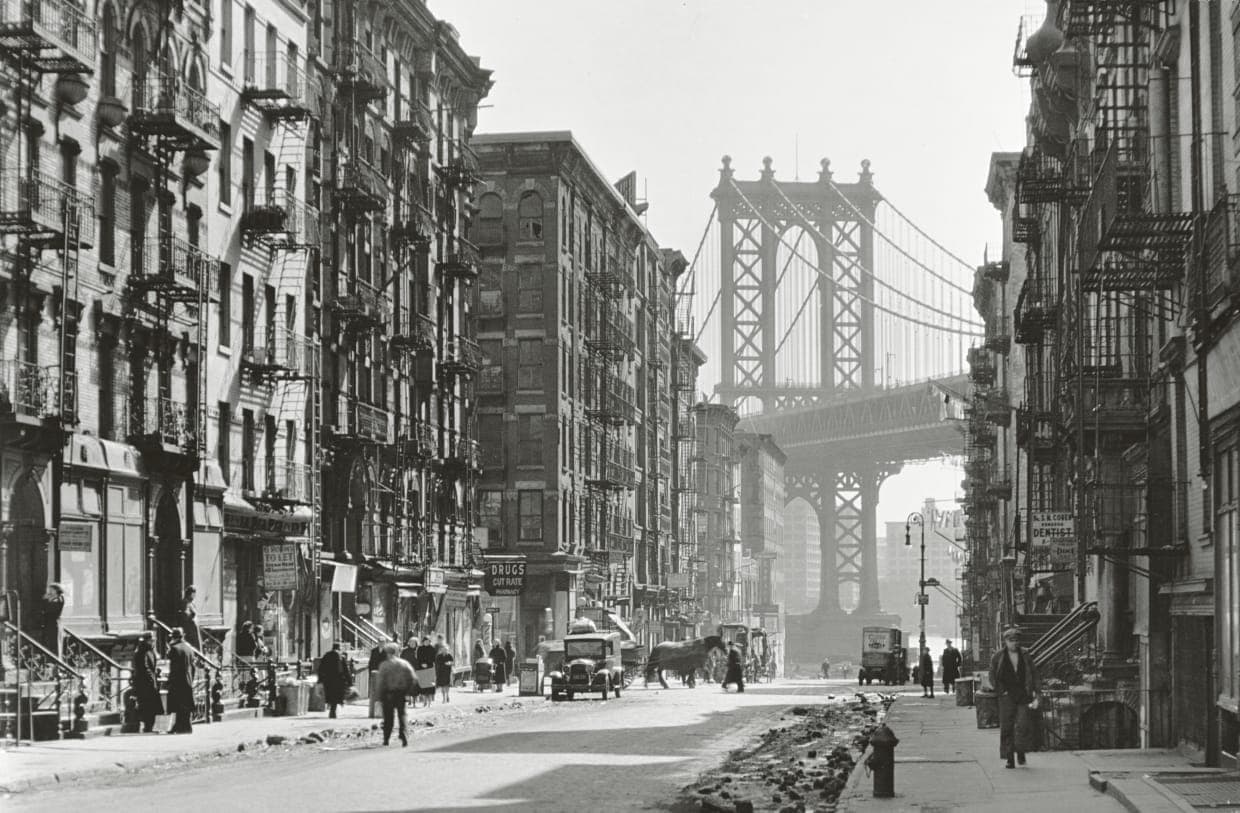 A New York street in the early 20th century, the Manhattan Bridge rising at the end of the block